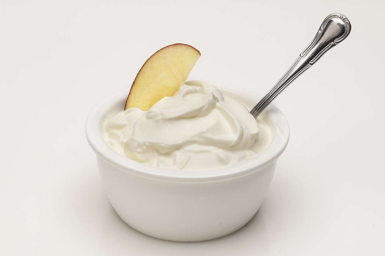 A bowl of Greek yogurt fruit dip has an apple slice and a spoon sticking out of it.