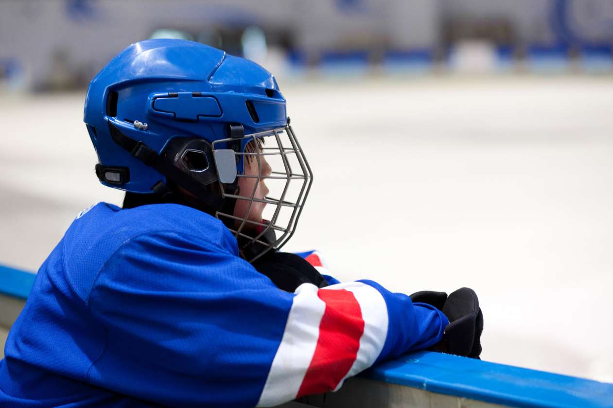 Boy wearing hockey helmet and uniform looks onto the ice