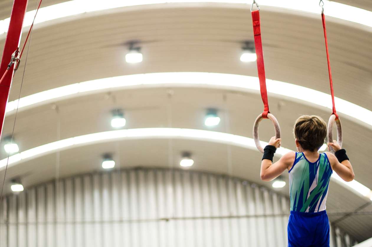 A boy hangs from the rings in a gymnastics gym.