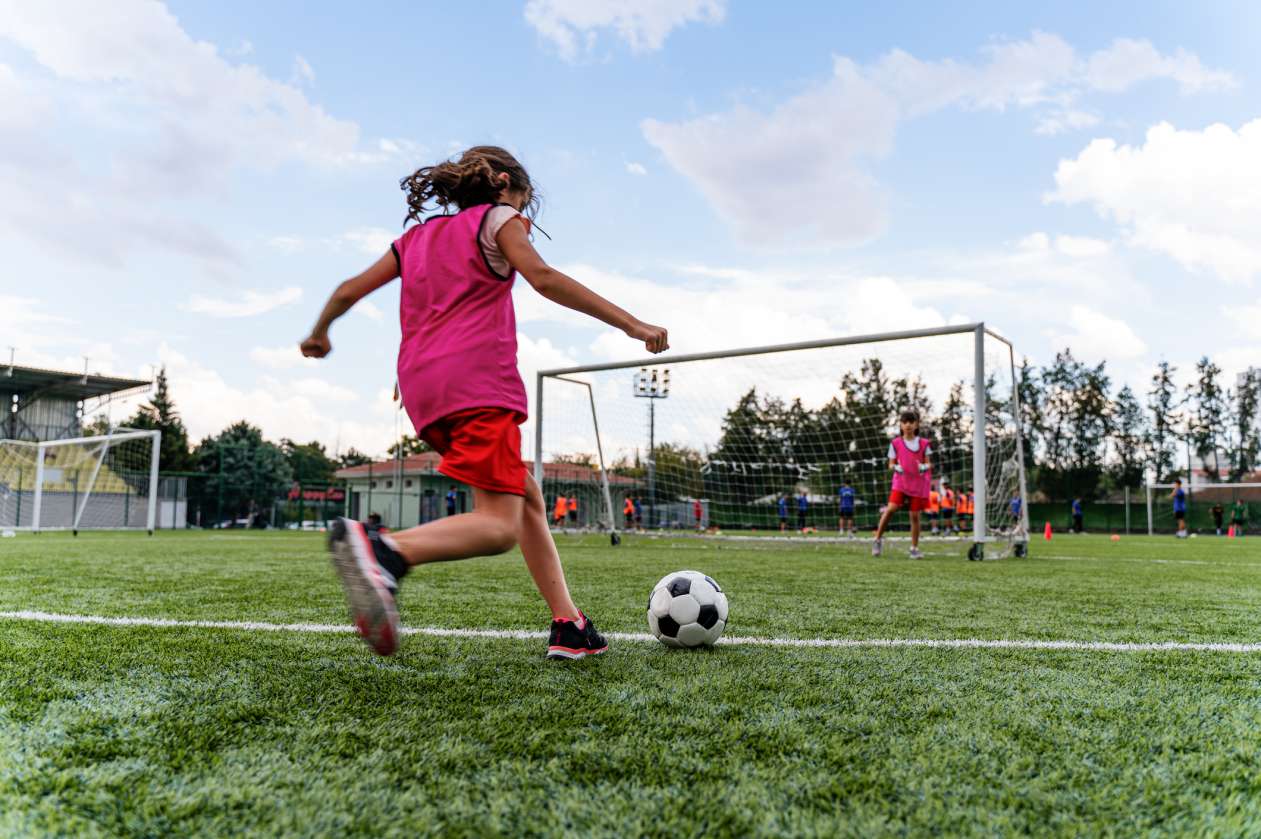 A girl kicks a soccer ball towards the net during a soccer game.