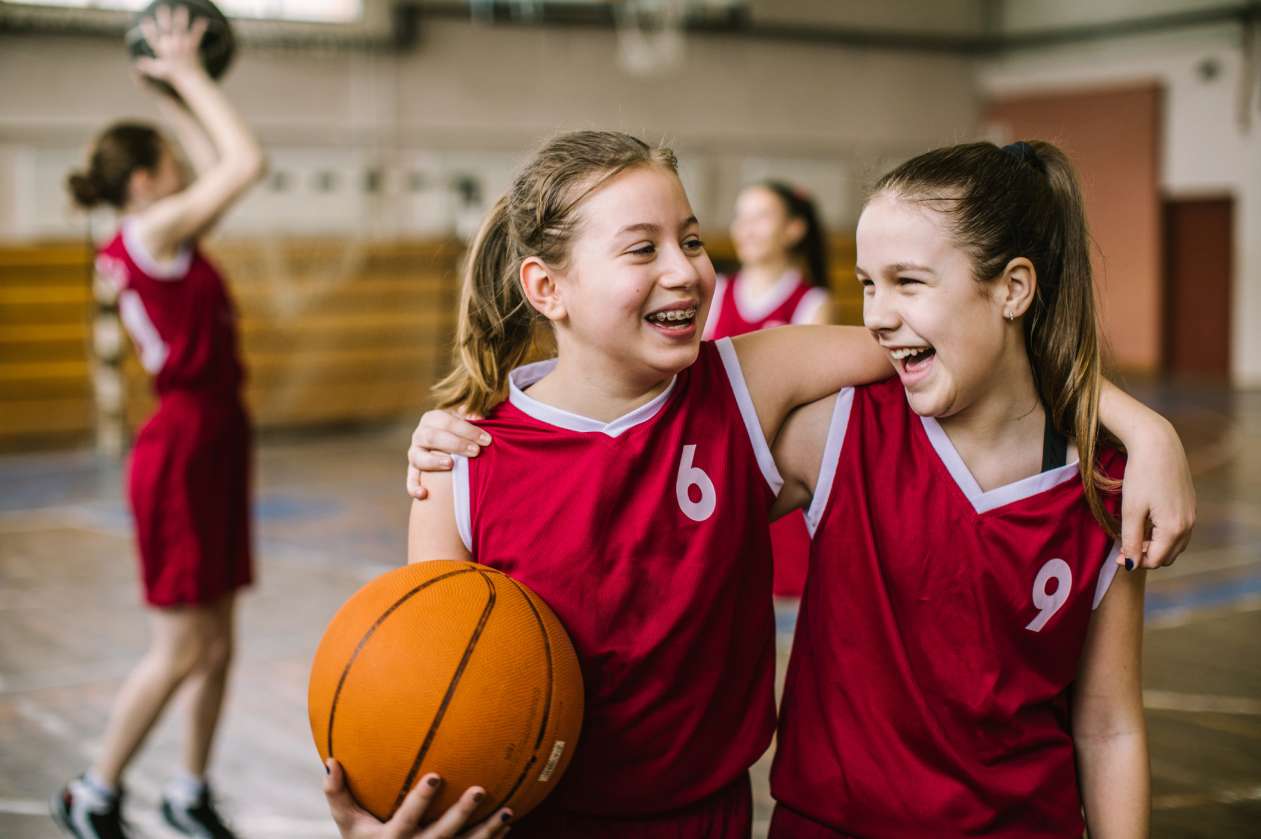 Two girls on a basketball court, with their arm around each other, laughing