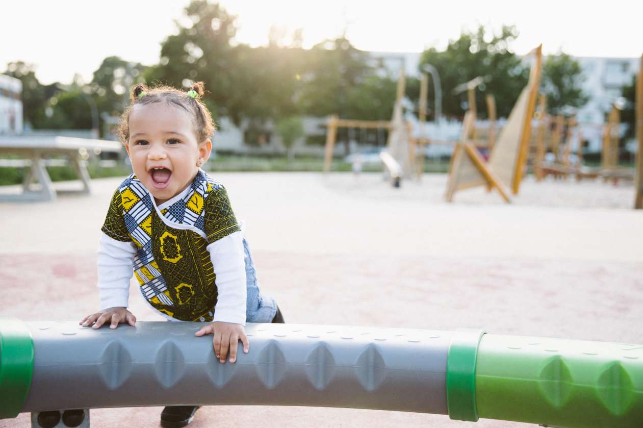 A smiling toddler plays on playground equipment outside.