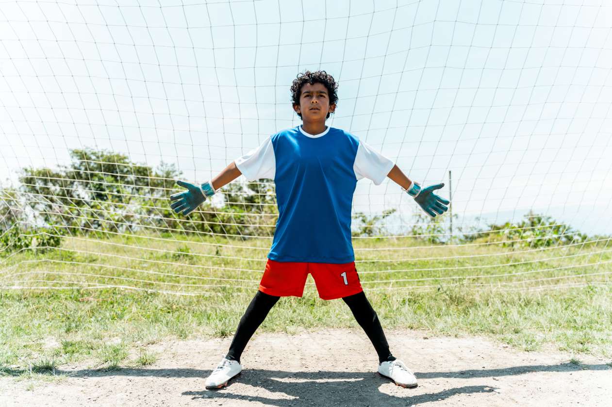 A boy stands in the middle of the net on a soccer field.