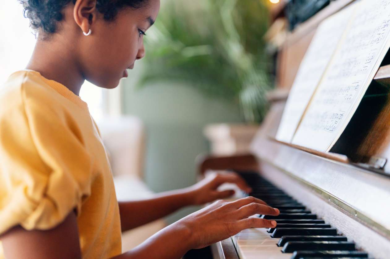 A girl sits at the piano, her hands over the keys.