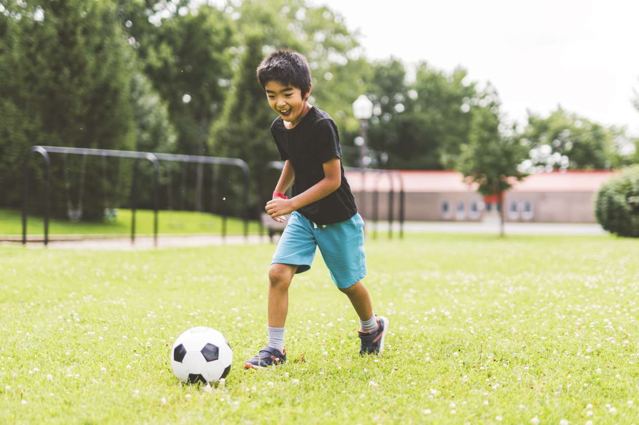 A boy runs down the soccer field, kicking the ball and laughing.