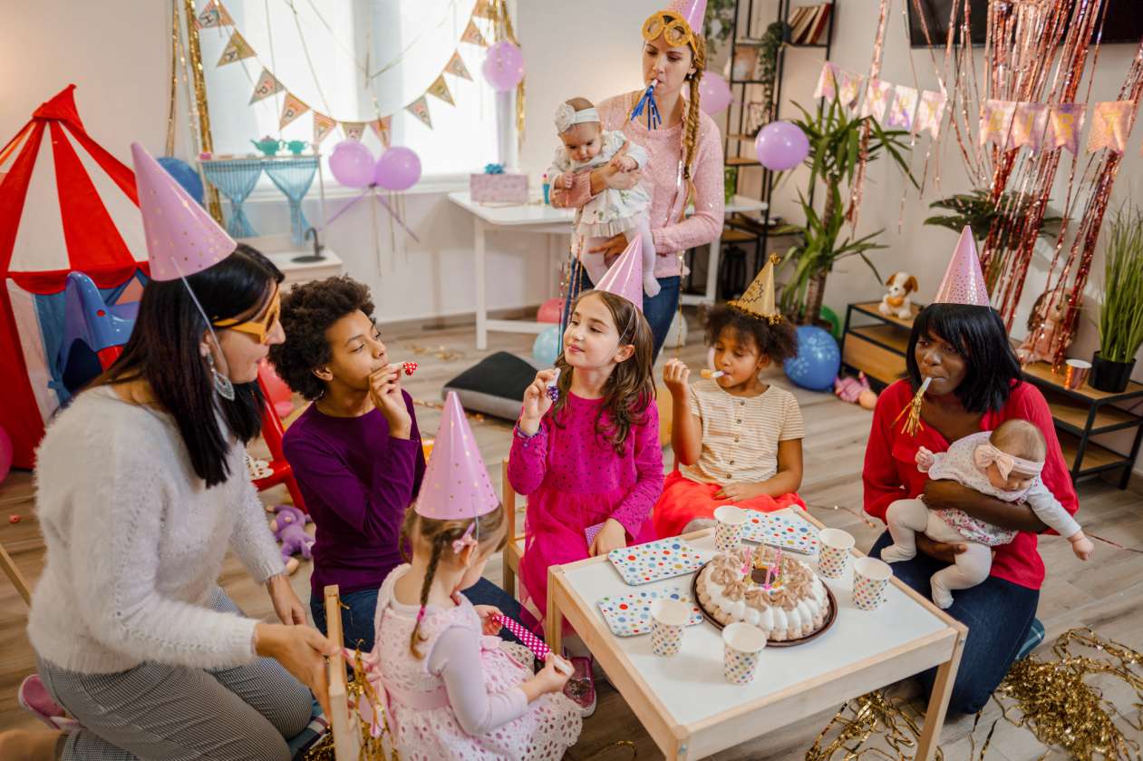 A group of moms and their kids celebrate a toddler's birthday party at home with birthday activities for kids.