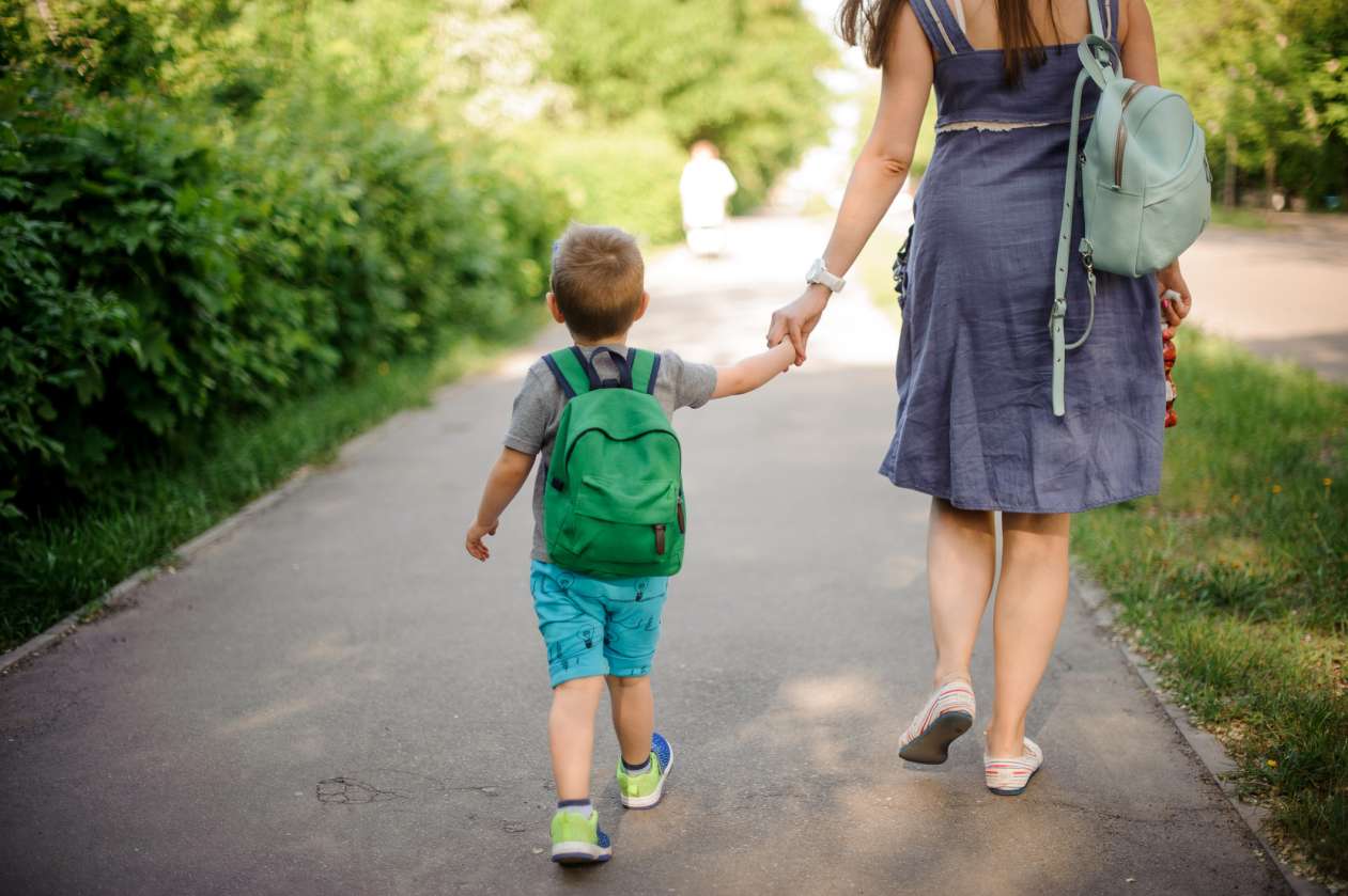 A kindergartener and his mom walk hand-in-hand to school.