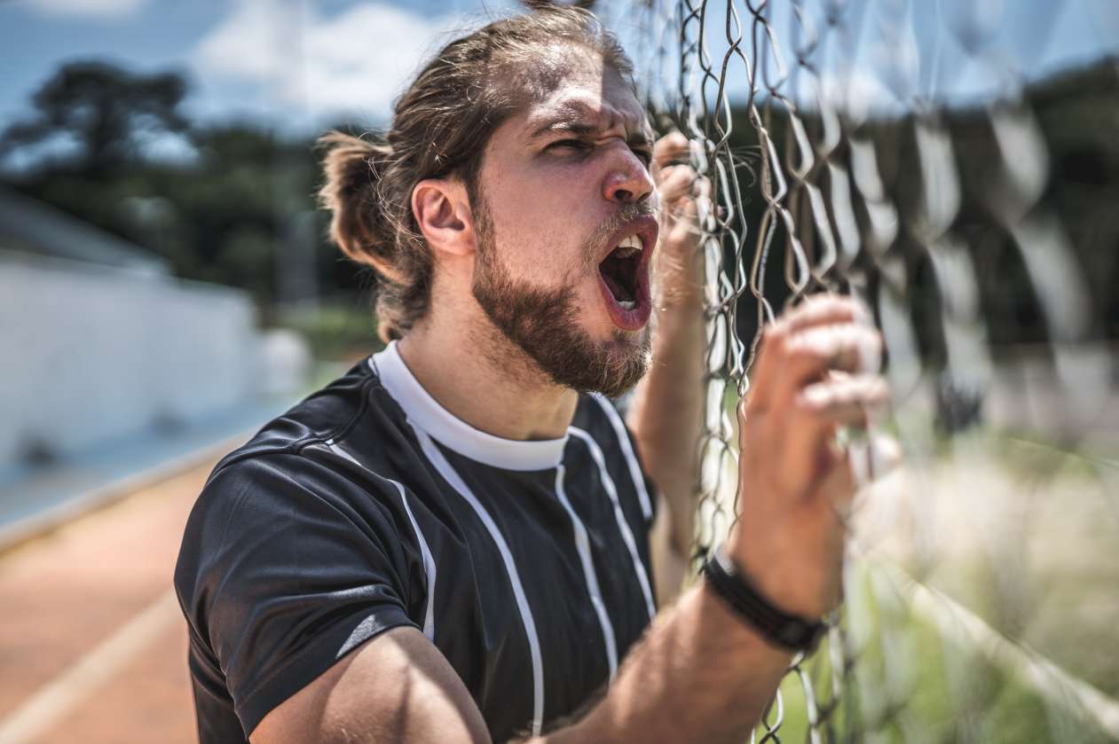 A dad grips the fence at a sports game and yells.