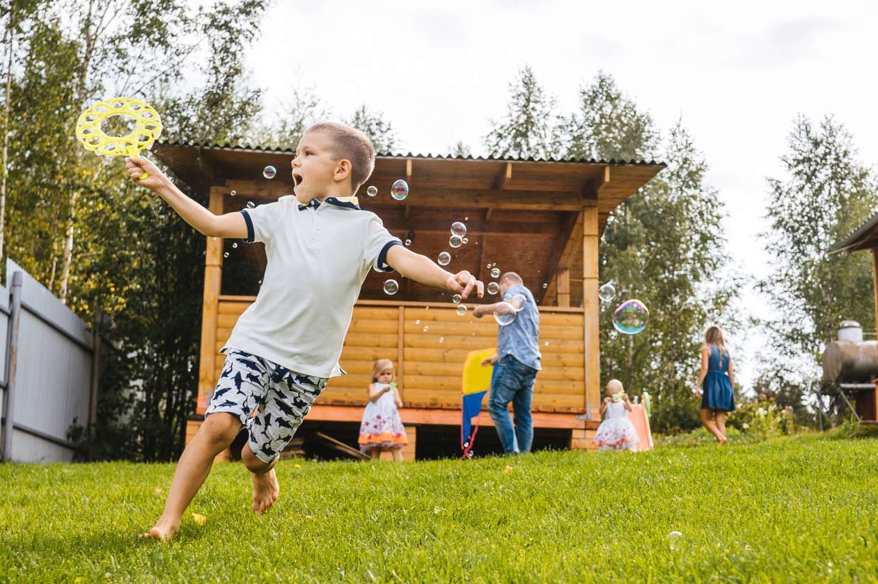A group of kids run and play with bubbles in a grassy backyard.
