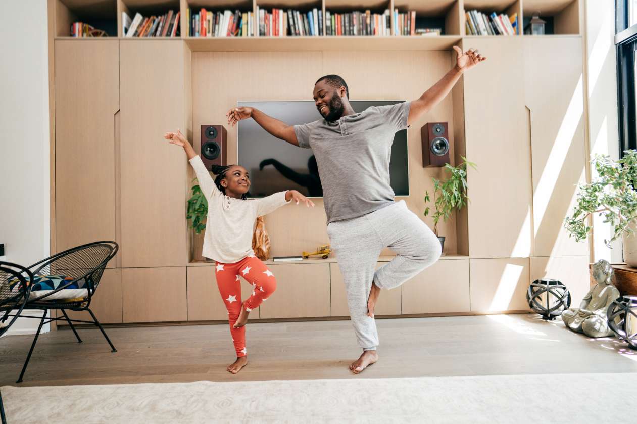 A father and his daughter do yoga together in the living room.