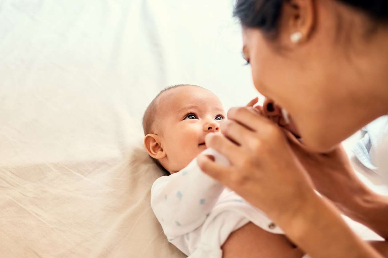 A mother smiles at her baby, who is lying on her back.