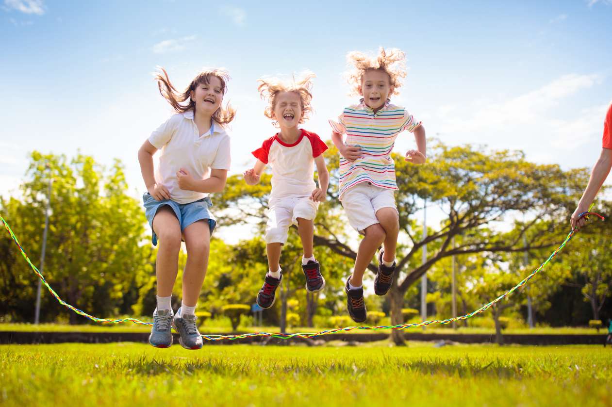 Three kids jump rope outside on a sunny, warm day.
