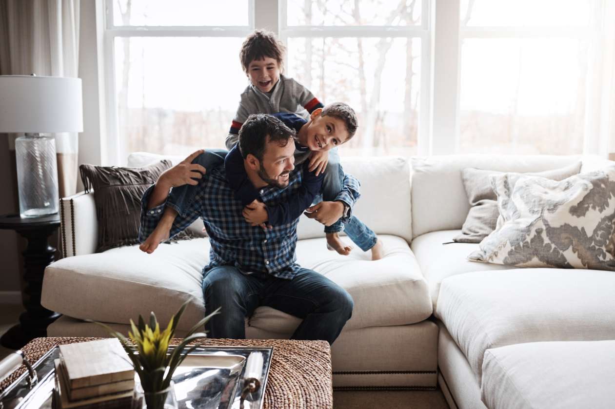 A dad and his two four-year-old sons rough house in the living room.