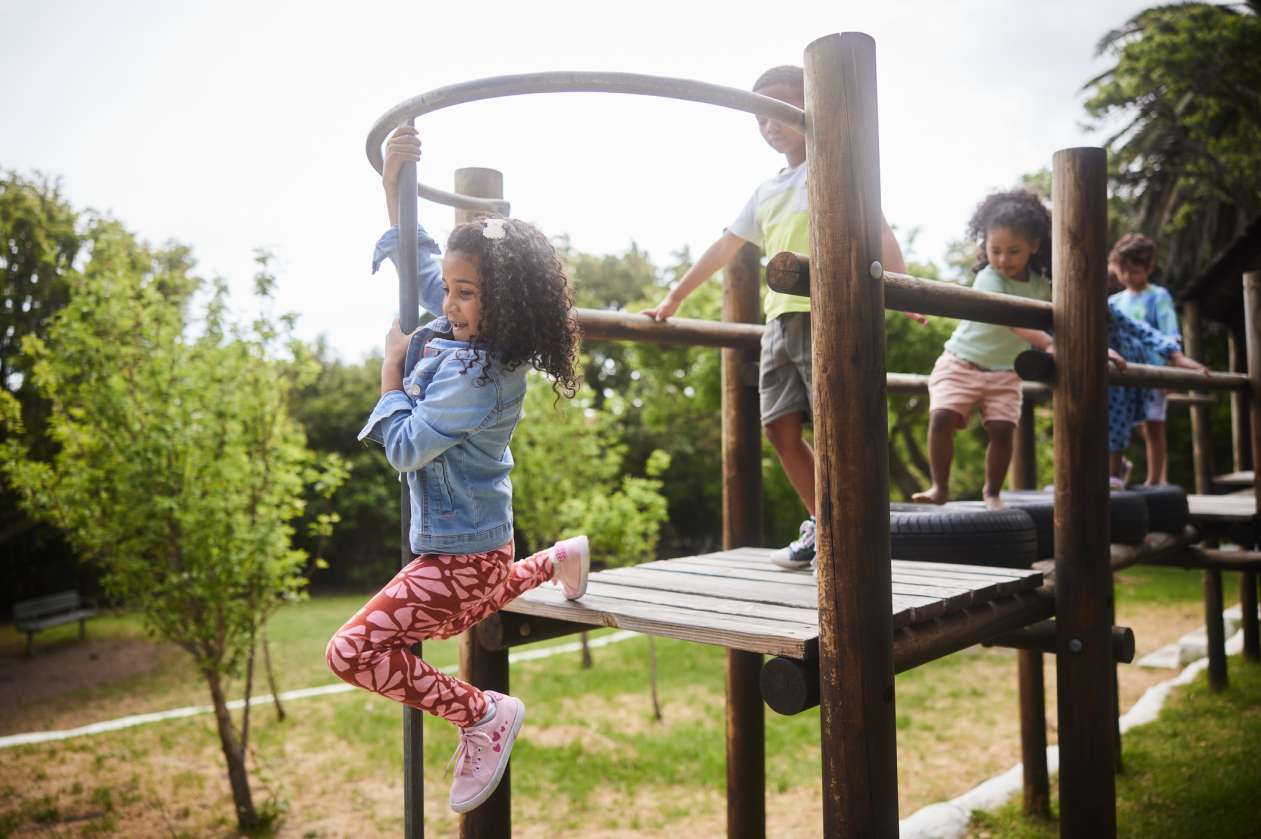 A group of kids laugh and play on a playground on a spring day.