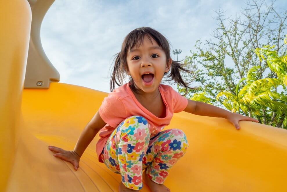 A young girl laughs as she goes down a playground slide.