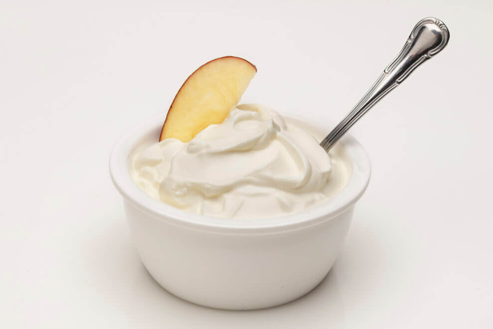 A bowl of Greek yogurt fruit dip has an apple slice and a spoon sticking out of it.
