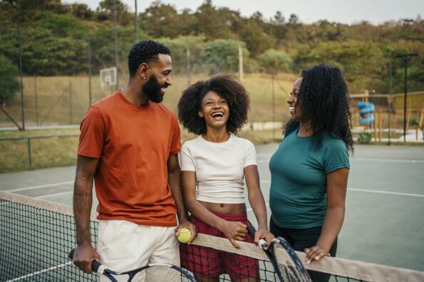A mom, dad, and their preteen daughter play tennis outdoors together.