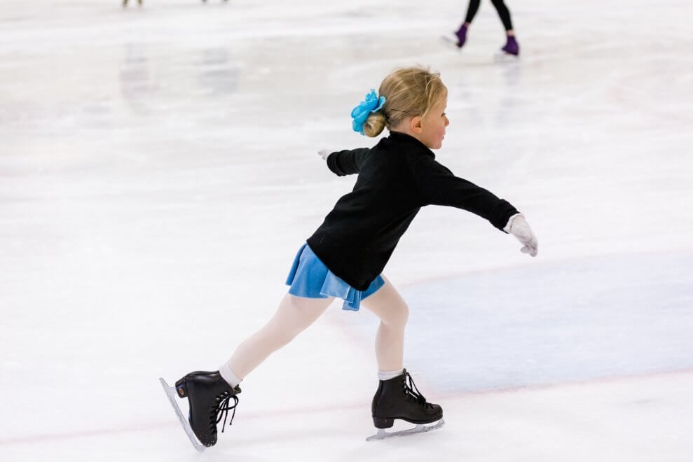 A young girl figure skates on an indoor ice rink.