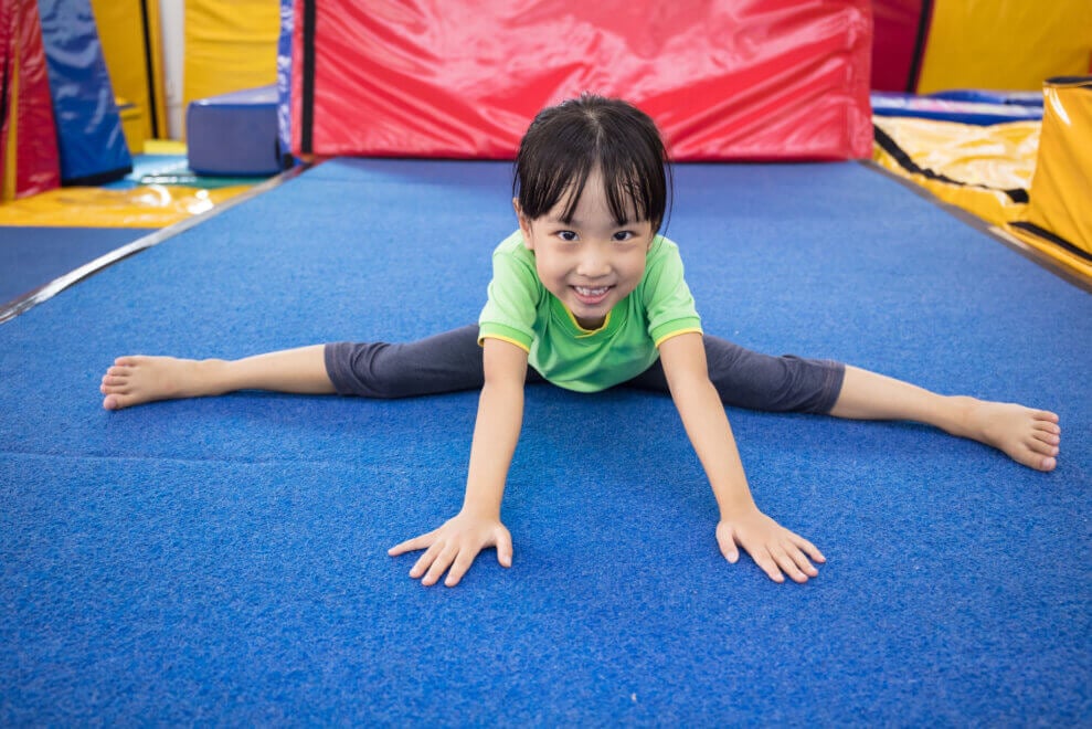 At a gymnastics gym, a little girl does the splits.