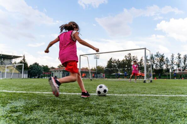 A girl kicks a soccer ball towards the net during a soccer game.