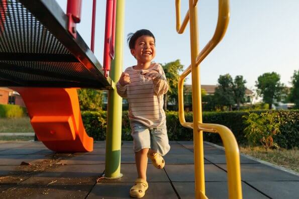 A young boy laughs as he runs around a playground on a sunny evening.