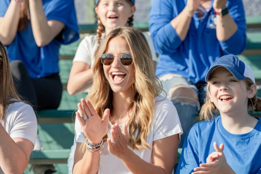 A mother and her daughter cheer on the bleachers at a kids' sports game.