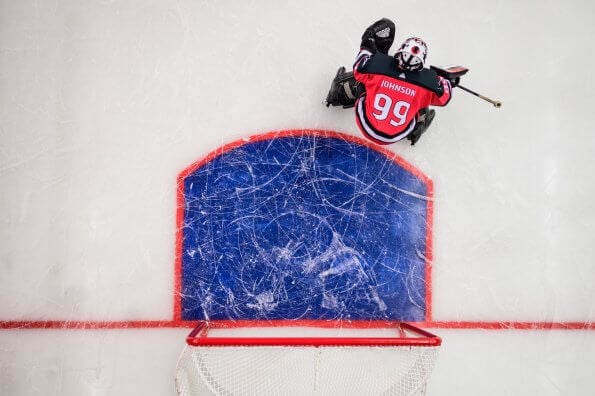 A hockey goalie waits in the net on the ice in an indoor rink.