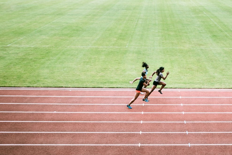 Three female athletes sprint around a track.