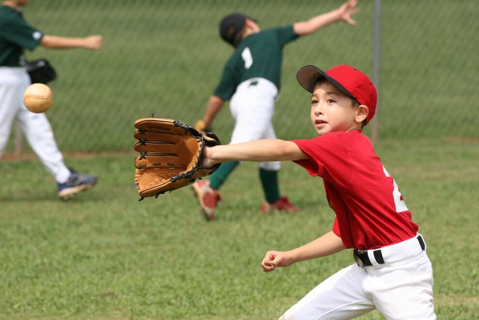 A boy reaches out to catch a baseball during a warm-up.