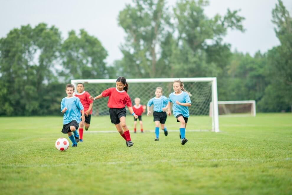 A girl kicks a soccer ball down the field during a game as players trail behind her.
