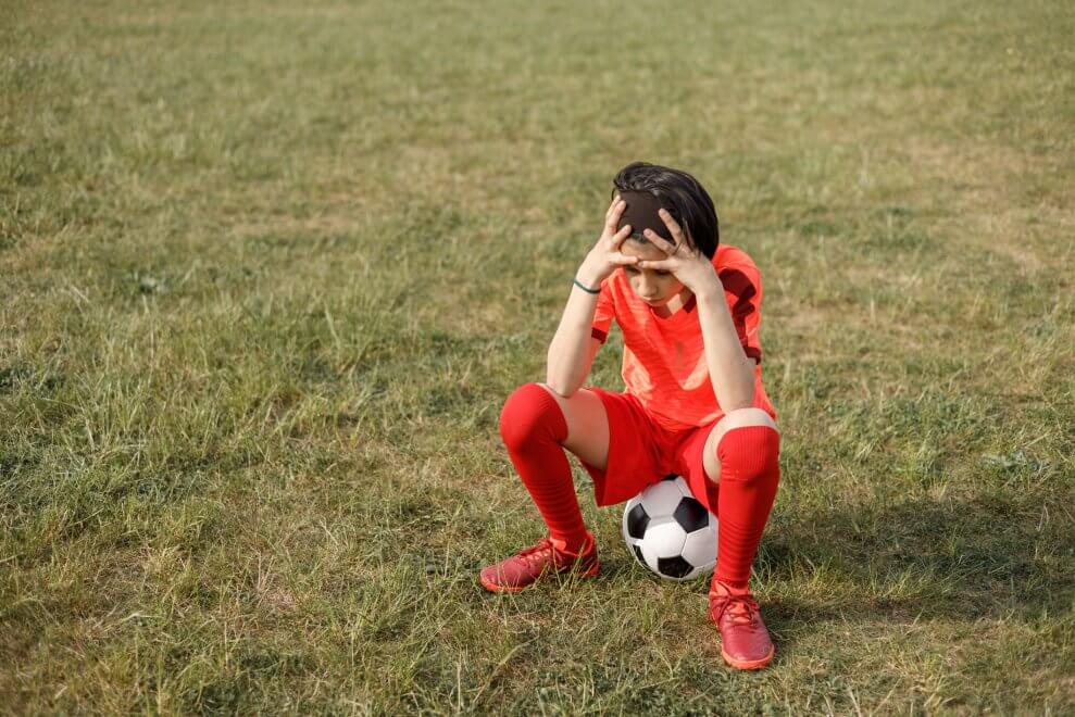 A girl sits on a soccer ball with her head in her hands.