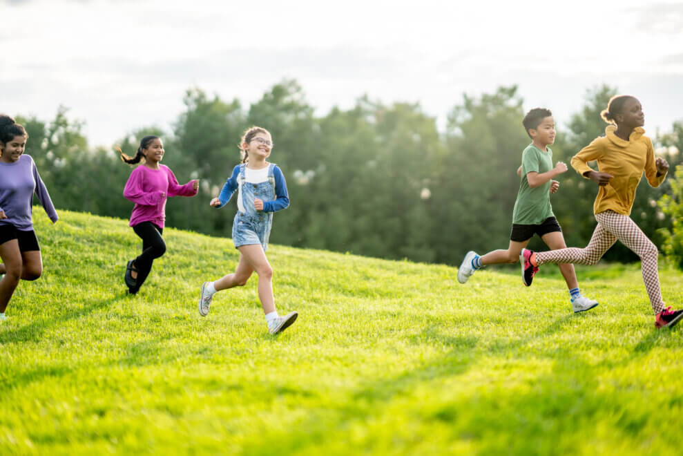A group of school-aged children run across a grassy field, laughing.