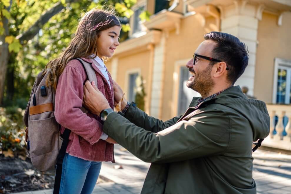 A dad crouches in front of his daughter and talks to her before she heads to school for the day.