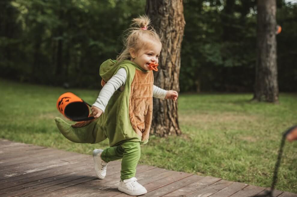 A toddler wears a green dinosaur costume for Halloween.