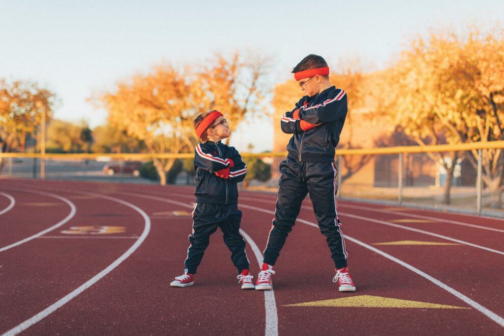 Two boys stand on a track, wearing track suits and sweatbands on their heads.