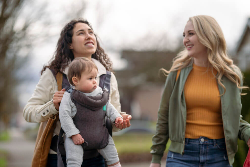 Two friends walking, one carrying her baby on her chest