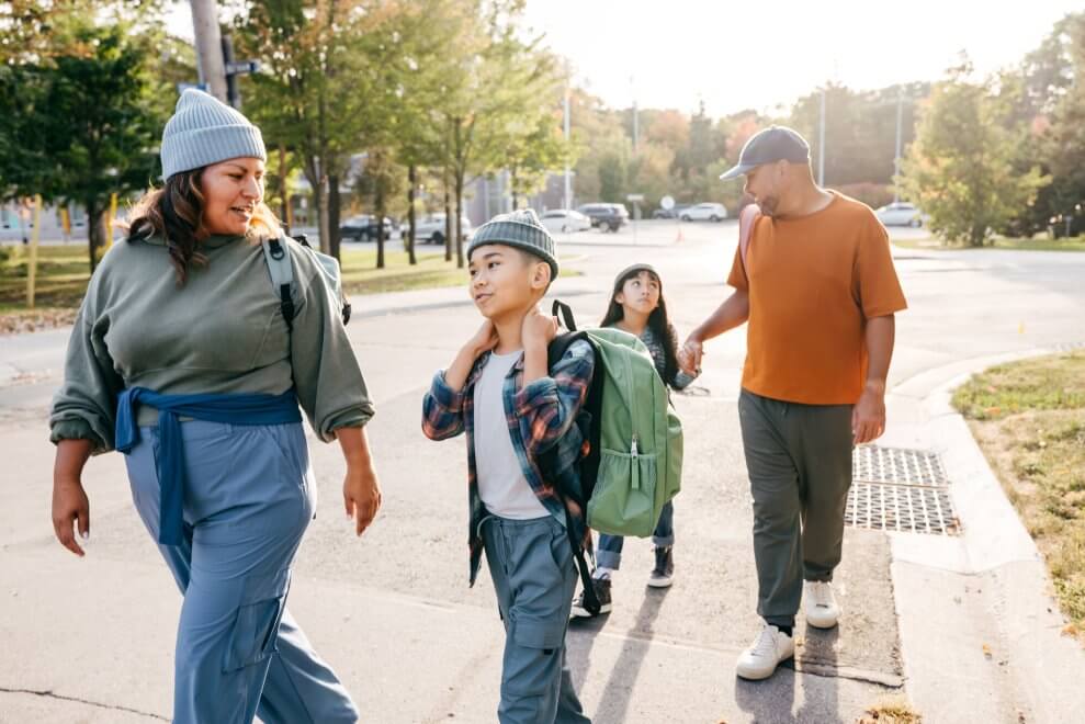 A mother, father, and their two children walk to school together on a sunny fall day.