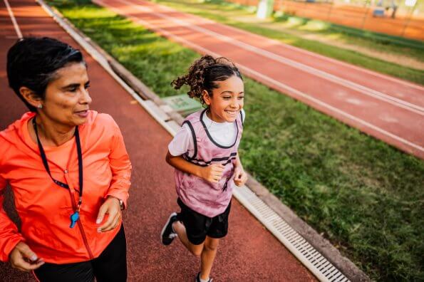 A smiling preteen girl runs with her coach around a track.