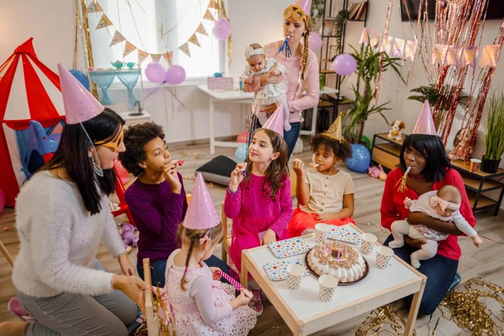 A group of moms and their kids celebrate a toddler's birthday party at home with birthday activities for kids.