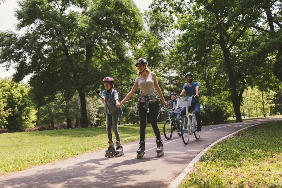 A mother and her daughter rollerblade through a park, while the father and son ride bikes behind them.