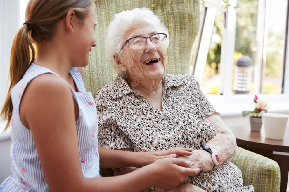 A granddaughter laughs with her grandmother in the living room.