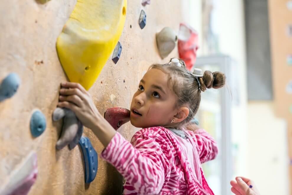 A girl boulders on a rock wall at an indoor climbing gym.