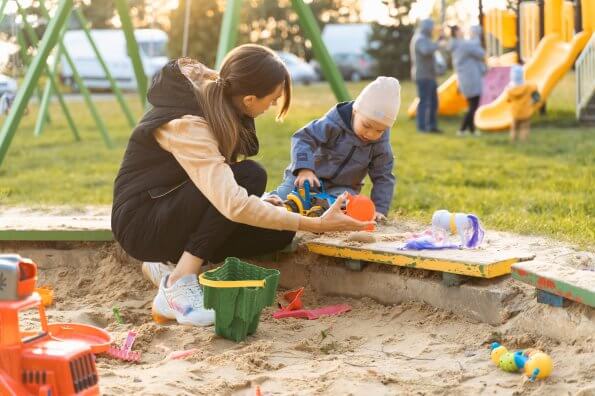 An ECE plays with a young child in the sandbox at a child care centre.