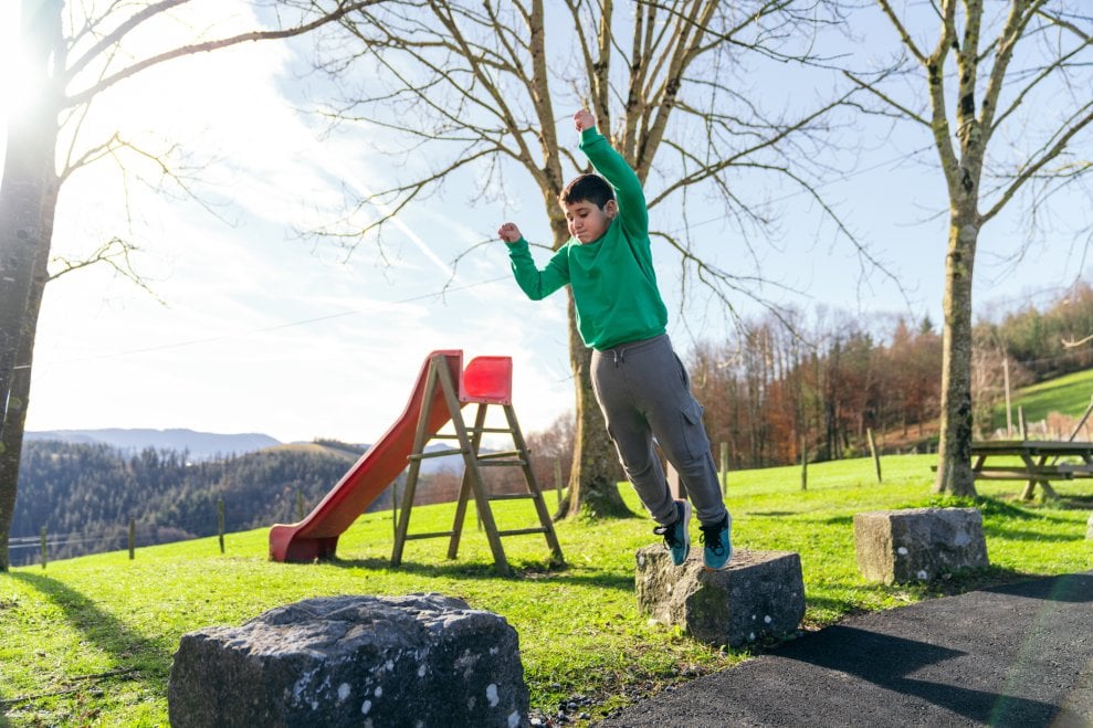 A boy jumps from one rock to the next in a playground on a sunny day.