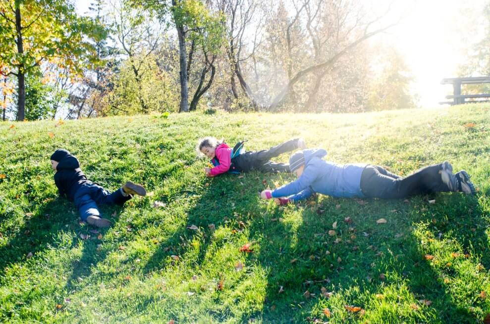 A mom and her two kids roll down a grassy hill on a sunny, autumn day.