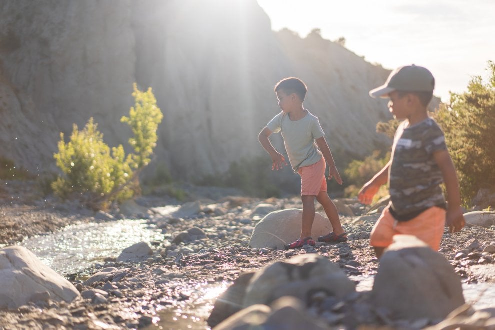 Two young boys throw stones into a shallow creek. 