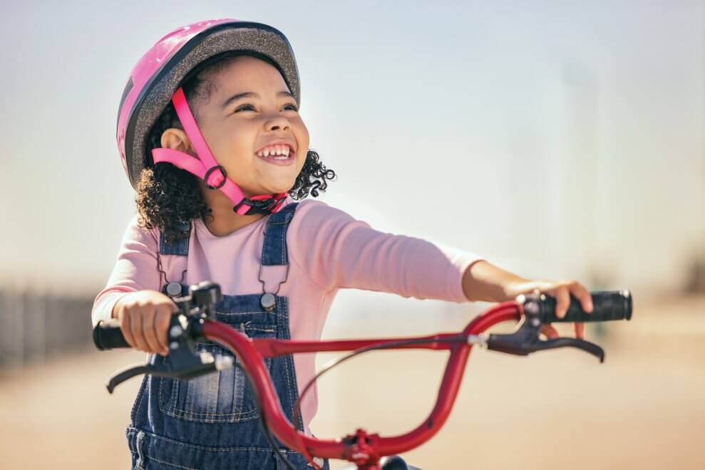 A smiling young girl walks alongside her bike on a sunny day.