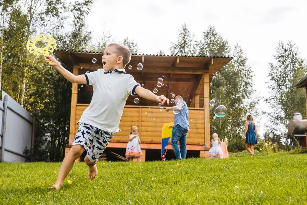 A group of kids run and play with bubbles in a grassy backyard.