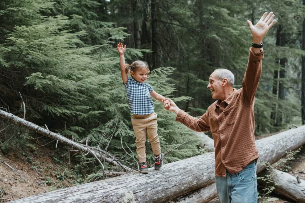 A young girl balances on a fallen log while she holds her dad's hand.