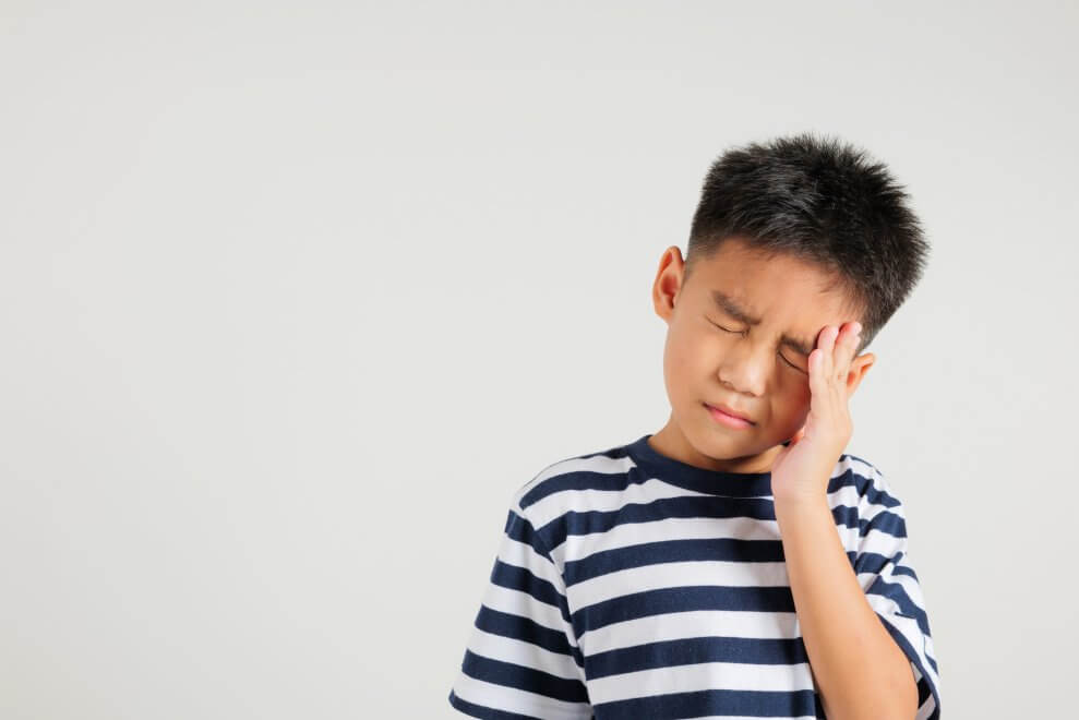 A young boy holds his head and grimaces in pain.
